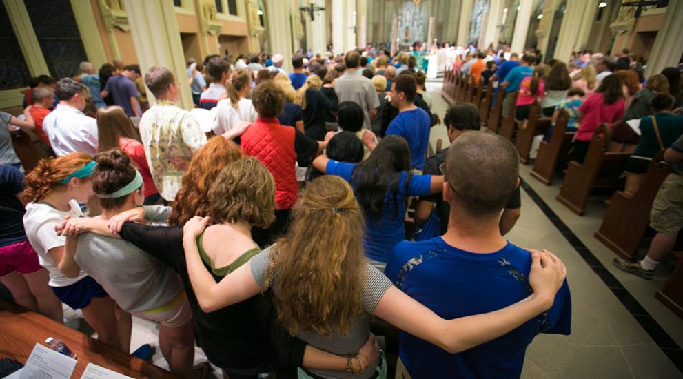 Students and families standing in unity in church with arms around each other.
