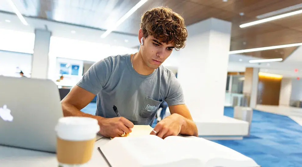 Student studying at table with book and laptop