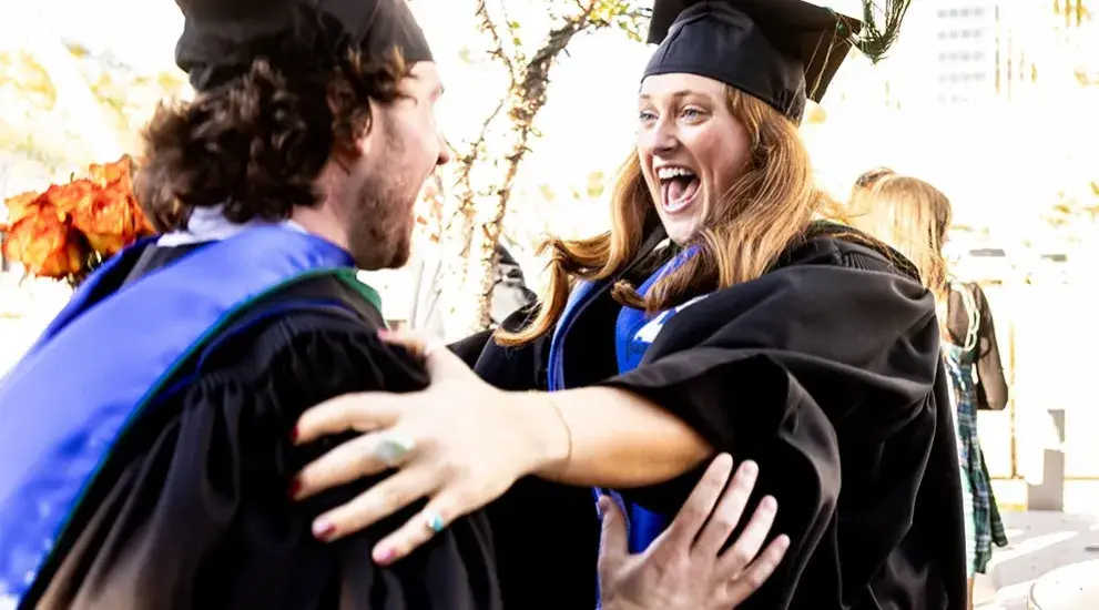 Students celebrating at commencement with a hug.