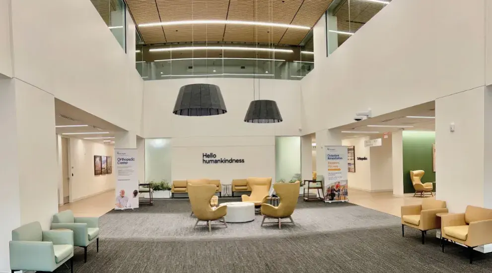 Interior view of the Orthopedic Center's spacious two-story lobby with contemporary furniture, large pendant lighting, and 'Hello humankindness' signage.